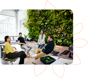 alt="Equipe reunida no escritório com parede verde com plantas"