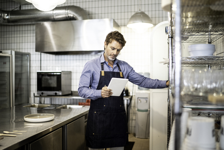 Homem dentro de uma cozinha industrial conferindo a lista de equipamentos para lanchonete