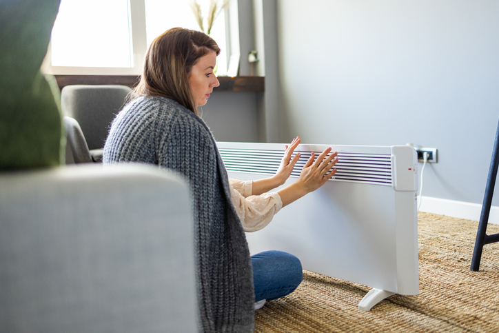 Mulher se aquecendo perto do aquecedor elétrico