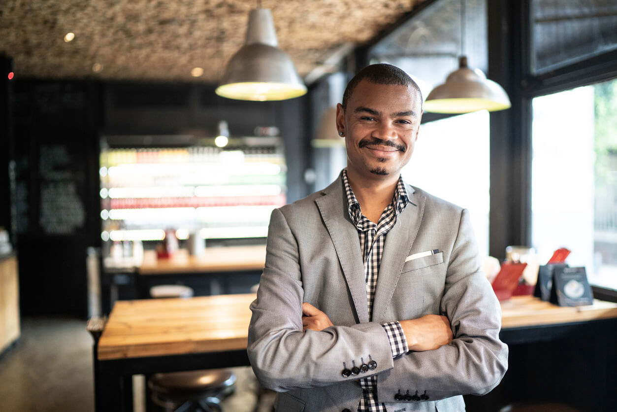 Dono da própria pizzaria sorrindo de braços cruzados no seu estabelecimento